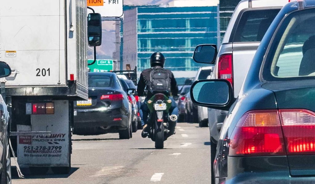 motorcycle riding between cars on road
