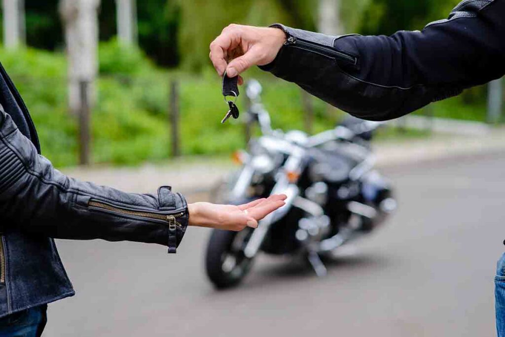 Man with gloves holding a key with motorcycle background.Motorcycle buying.